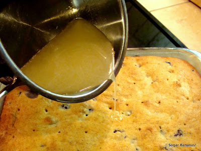 melted lemon mixture being pour out of a pot over the berry cake punched with holes in a baking pan on www.sugarbananas.com